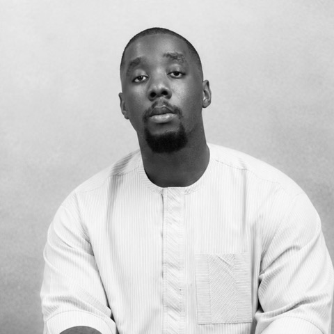Arnold Ikpemosi in a white kaftan, looking at the camera.